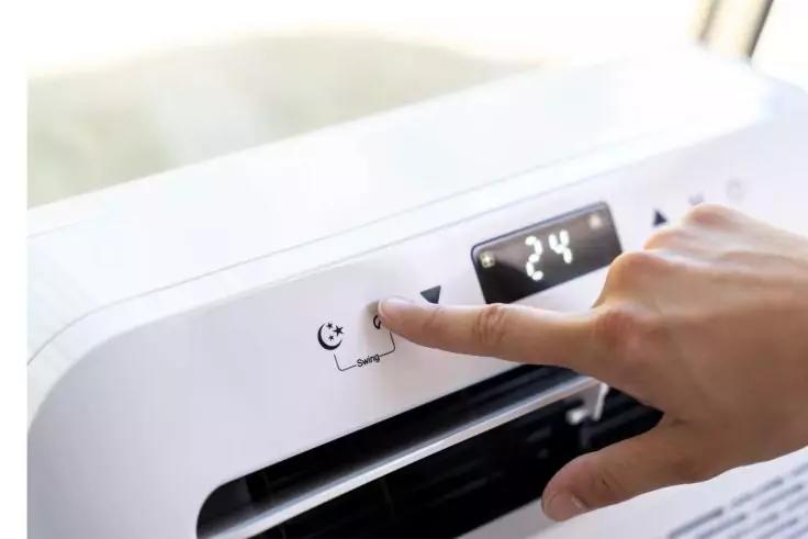 Hand mit ausgestrecktem Zeigefinger drückt einen Knopf an einem weißen Gerät mit Luftauslass und schwarzem Display, auf dem '24' steht