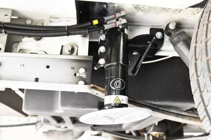 Unterboden eines Fahrzeugs mit schwarzem zylindrischem Bauteil mit Aufkleber, Metallrahmen, Kabeln und rechtem Reifen