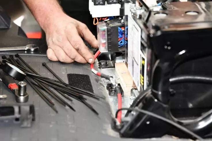 Hand &uuml;ber einem ge&ouml;ffneten elektronischen Ger&auml;t, sichtbare rote und schwarze Kabel, mehrere Kabelbinder auf der Arbeitsfl&auml;che