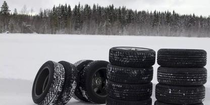 Mehrere Autoreifen auf einer verschneiten Fl&auml;che, einige gestapelt, im Hintergrund B&auml;ume und bew&ouml;lkter Himmel