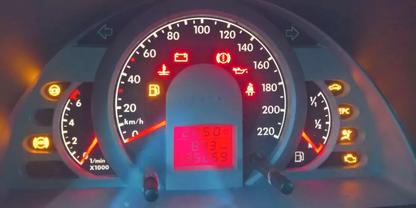 Fahrzeug-Instrumententafel mit mittigem Tachometer (Skala bis 200 km/h), Drehzahlmesser links, Kraftstoff- und Temperaturanzeige rechts, mittig rotes digitales Display und mehrere gelbe und rote Warnsymbole leuchtend