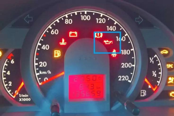 Instrumententafel eines Autos mit zentralem Tachometer (0&ndash;220 km/h), linkem Drehzahlmesser, rechter Kraftstoffanzeige, rotem digitalen Display unten und mehreren roten und gelben leuchtenden Symbolanzeigen (Batterie, &Ouml;lsymbol, Reifen/ Ausrufezeichen,