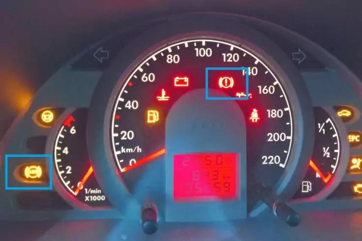 Armaturenbrett eines Autos mit zentralem Tacho (km/h), links Drehzahlmesser, mittig rotes digitales Display und mehrere gelb/rot leuchtende Warnsymbole (Batteriesymbol, Ausrufezeichen in Kreis, Sicherheitsgurt-Symbol, Motorsymbol)