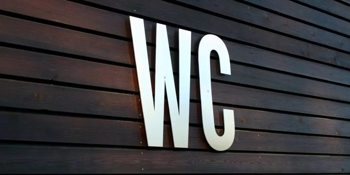 Wei&szlig;e Gro&szlig;buchstaben 'WC' auf dunkelbraunen, horizontalen Holzlatten