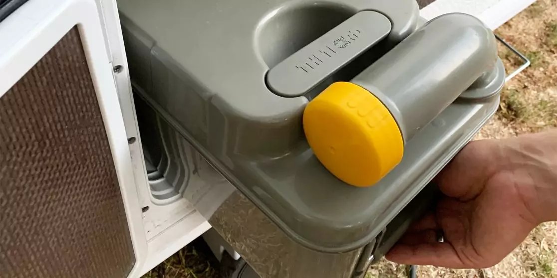 Hand h&auml;lt grauen Kunststoffbeh&auml;lter mit rundem gelben Verschluss neben einer wei&szlig;en &Ouml;ffnung mit L&uuml;ftungsgitter