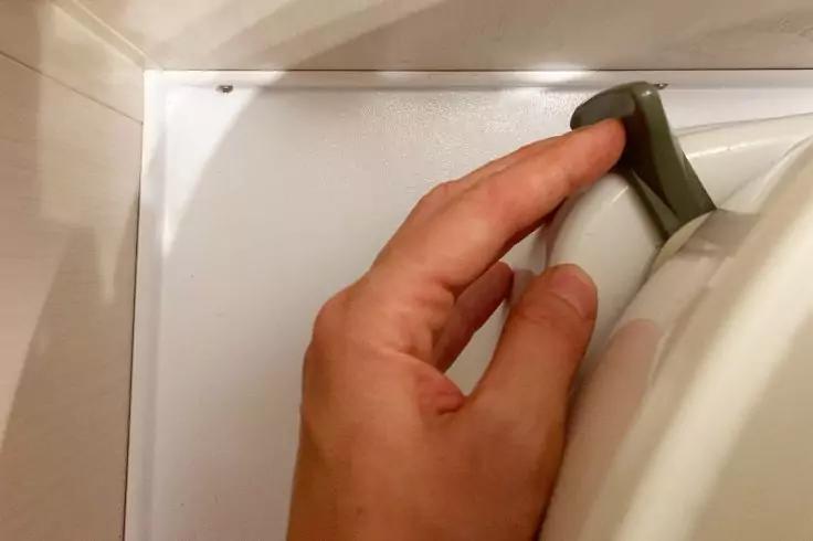 Hand greift einen grauen Griff an der weißen Tür eines Geräts