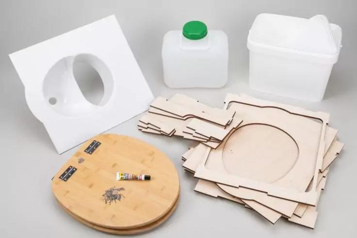 Stapel zugeschnittener Sperrholzplatten mit runden Ausschnitten, rundes Holzbrett mit kleinen Metallteilen und Klebestift, zwei wei&szlig;e Kunststoffbeh&auml;lter (einer mit gr&uuml;nem Verschluss) und ein wei&szlig;es Kunststoffteil mit gro&szlig;em rundem Ausschnitt auf neut