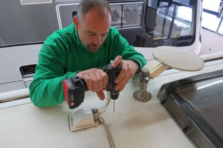 Person in gr&uuml;nem Pullover h&auml;lt schwarzen Akkuschrauber &uuml;ber wei&szlig;e Arbeitsfl&auml;che neben Sp&uuml;le und Fenster