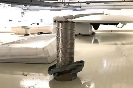 Flexibles, gewelltes Metallrohr steht senkrecht in einer runden &Ouml;ffnung auf einer gl&auml;nzend wei&szlig;en Fl&auml;che; am Rohrfu&szlig; eine Metallbandage, im Hintergrund zwei durchsichtige Kuppeln und Deckenleitungen