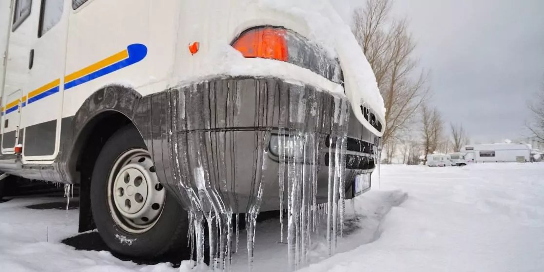 Front eines Wohnmobils mit Eiszapfen am Sto&szlig;f&auml;nger, Schnee am Boden und Rad sichtbar