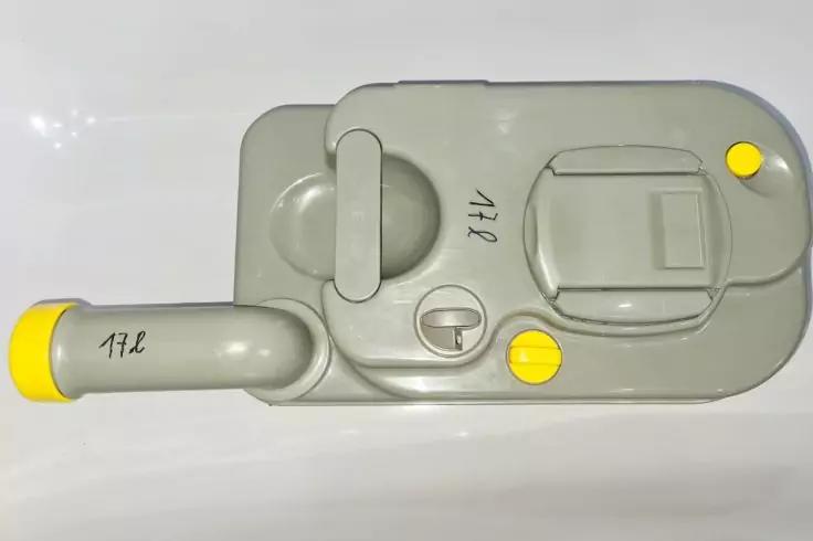 Graues Plastikteil mit kurzem gebogenem Rohr, drei gelben Abdeckkappen und handschriftlicher Beschriftung '17L' auf der Oberfl&auml;che