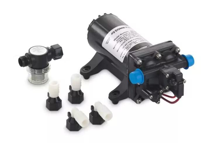 Kleine schwarze elektrische Pumpe mit Aufkleber, zwei blauen Schutzkappen an den Anschlussstutzen, rote und schwarze Kabel; daneben mehrere wei&szlig;e und schwarze Kunststoffanschl&uuml;sse und ein schwarzes Bauteil mit durchsichtigem oberen Teil