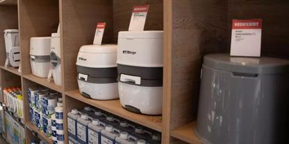 Holzregal mit mehreren wei&szlig;en und grauen runden K&uuml;chenger&auml;ten, Produktk&auml;rtchen oben, Dosen und Verpackungen auf den unteren Regalb&ouml;den