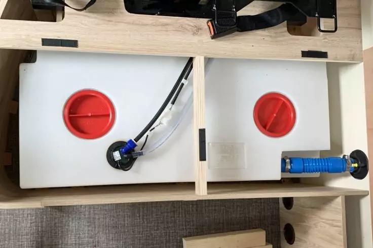 Holzfach mit zwei wei&szlig;en Kunststoffbeh&auml;ltern, jeweils roter Schraubverschluss; Schl&auml;uche mit schwarzen und blauen Anschl&uuml;ssen sichtbar