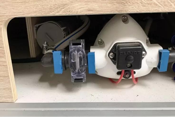 Innenseite eines Schranks mit rundem wei&szlig;en Kunststoffgeh&auml;use, schwarzem rechteckigem Bauteil mit roten und schwarzen Kabeln, durchsichtigem Sicherungshalter mit blauen Steckverbindern, grauen Kabeln und Holzverkleidung