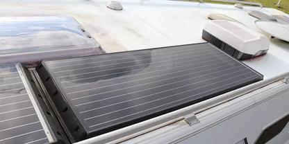 Dunkles, rechteckiges Solarpanel mit feinen Linien auf wei&szlig;em Fahrzeugdach; links weiteres Panel, oben zwei wei&szlig;e Dachaufbauten und kleine Antenne