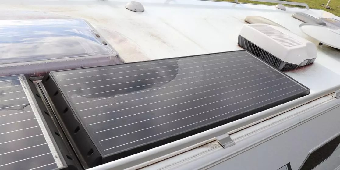 Dunkles, rechteckiges Solarpanel mit feinen Linien auf wei&szlig;em Fahrzeugdach; links weiteres Panel, oben zwei wei&szlig;e Dachaufbauten und kleine Antenne