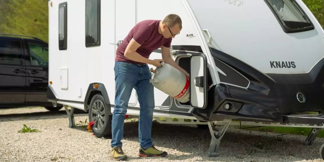 Mann hebt eine Gasflasche in das vordere Staufach eines Wohnwagens