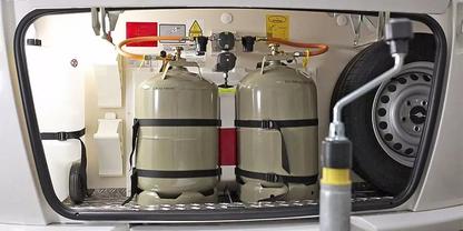 Staufach mit zwei grauen Metallgasflaschen nebeneinander, oben angeschlossene Schl&auml;uche und Regler, rechts Reserverad, vorne ein graues Rohr mit gelbem Griff