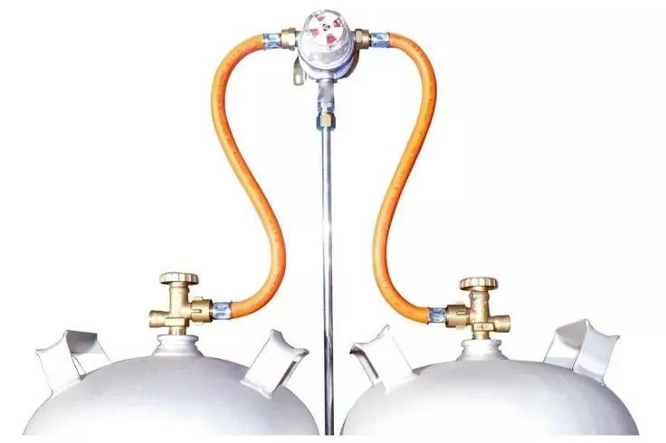 Zwei Metallflaschen (obere Teile) mit Ventilgriffen, durch orange Schläuche mit einem zentralen Gerät mit rundem Messgerät verbunden