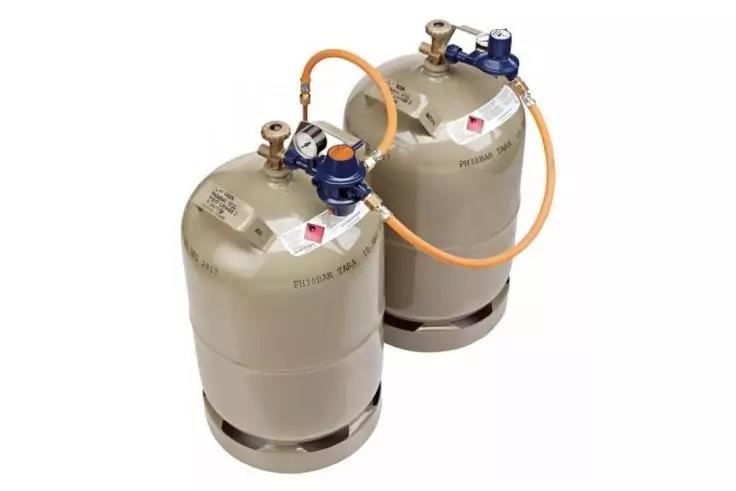 Zwei graue Gasflaschen, durch einen orangefarbenen Schlauch verbunden, mit sichtbaren Ventilen