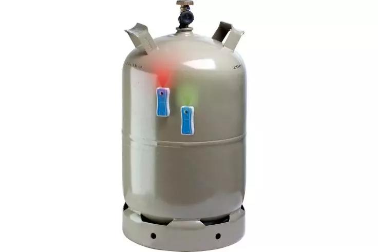 Zylindrischer silberner Metallbeh&auml;lter auf rundem Sockel, Ventil oben, zwei kleine blaue Aufkleber an der Seite, rote und gr&uuml;ne Lichtreflexe auf der Oberfl&auml;che