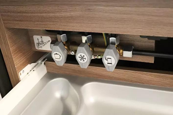 Drei graue Kunststoffgriffe mit Symbolaufklebern (Steckdose, Schneeflocke, Becher) an einer Metallstange unter einem Holzpaneel &uuml;ber einer wei&szlig;en Sp&uuml;le