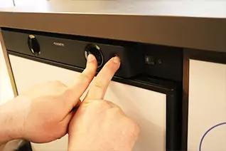 Zwei H&auml;nde greifen einen schwarzen Drehknopf an der Front eines wei&szlig;en K&uuml;chenger&auml;ts