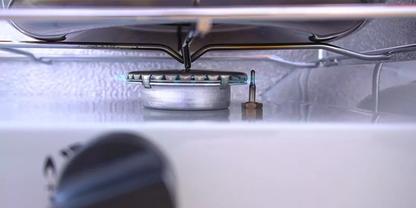 Metallinnenraum mit rundem gelochtem Bauteil in der Mitte, Metallgitter dar&uuml;ber, vertikaler Metallstift seitlich und unscharfer schwarzer Drehknopf im Vordergrund