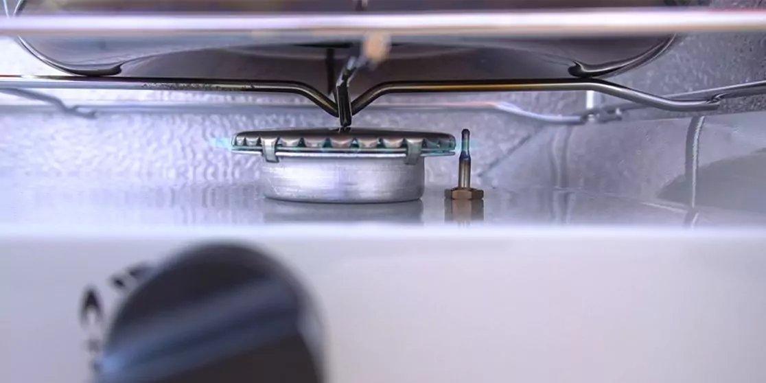 Metallinnenraum mit rundem gelochtem Bauteil in der Mitte, Metallgitter dar&uuml;ber, vertikaler Metallstift seitlich und unscharfer schwarzer Drehknopf im Vordergrund