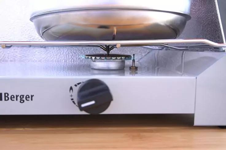 Nahaufnahme eines Kochers mit Metalltopf auf dem Brenner, sichtbare Flamme, vorderer Drehregler und Schriftzug "Berger", Ger&auml;t auf Holzoberfl&auml;che