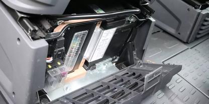 Offenes Kunststofffach mit zwei rechteckigen Modulen mit Etiketten, sichtbaren Kabeln und einem abgenommenen Gitter auf grauem, geriffeltem Boden