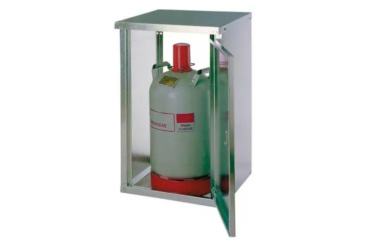Offener Metallschrank mit darin stehender grauer Gasflasche, roter Ventilkappe und rotem Sockel, sichtbares Etikett