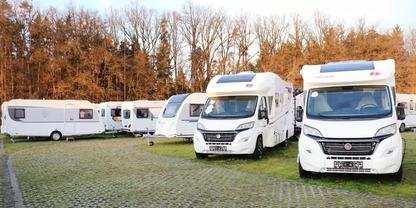 Mehrere wei&szlig;e Wohnmobile auf einem gepflasterten Stellplatz mit grasbewachsenen Gittersteinen, im Hintergrund kahle B&auml;ume, keine Personen