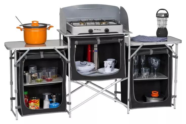 Klapptable K&uuml;chenstation mit zweiflammligem Herd oben, orangefarbener Kochtopf mit Deckel links, Laterne und Tuch rechts; darunter drei offene Stofff&auml;cher mit Tellern, Tassen, Gl&auml;sern, Dose und rotem zylindrischem Beh&auml;lter