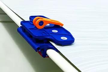 Blaue Kunststoffklemme mit orangefarbenem Hebel, befestigt an weißer, welliger Platte und weißem Rundrohr