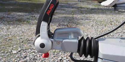 Nahaufnahme einer Anh&auml;ngerkupplung mit schwarzem Hebel, silbernem Kupplungskopf, gummiertem Faltenbalg und Kiesboden