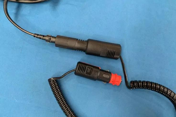 Schwarzes spiralförmiges Kabel mit schwarzem Auto-Stromstecker mit rotem Kunststoffende und schwarzem Inline-Stecker auf blauem Hintergrund