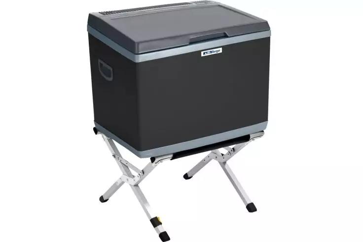 Dunkelgrauer, rechteckiger Kasten mit hellgrauem Deckel und heller Zierleiste, steht auf einem X-förmigen Metallgestell mit vier Beinen; seitliche Griffe und kleines rechteckiges Etikett vorne sichtbar