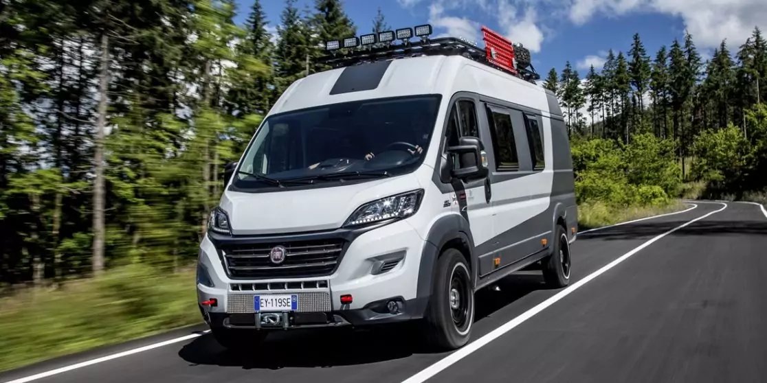 Wei&szlig;es Wohnmobil auf einer asphaltierten Landstra&szlig;e, rechts und links B&auml;ume, blauer Himmel mit einzelnen Wolken