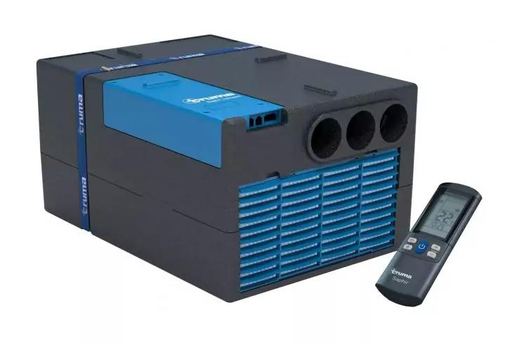 schwarzes rechteckiges Ger&auml;t mit blauem L&uuml;ftungsgitter vorne, drei runden Ausl&auml;ssen oben rechts und einer grauen Fernbedienung rechts neben dem Ger&auml;t