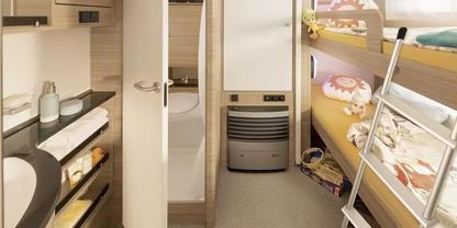 Raum mit Etagenbetten rechts, Metallleiter und Bettw&auml;sche; mittig ein Heizger&auml;t; links Waschbecken, Handtuch und offene Schr&auml;nke mit Geschirr