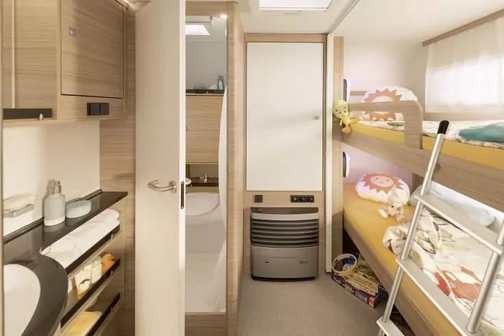 Innenraum mit Etagenbetten rechts, Leiter, Kuscheltiere, Regale und Waschbecken links, Tür zum Bad und Heizgerät am Ende