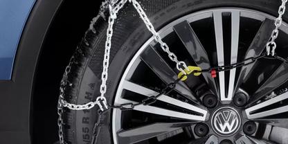 Nahaufnahme eines mit Schneeketten versehenen VW-Rads: Felge, Reifen, Kettenglieder, gelb-rote Spannhaken und blauer Kotfl&uuml;gel