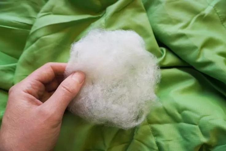 Hand h&auml;lt einen kleinen wei&szlig;en, fusseligen Faserball auf gr&uuml;nem Stoff