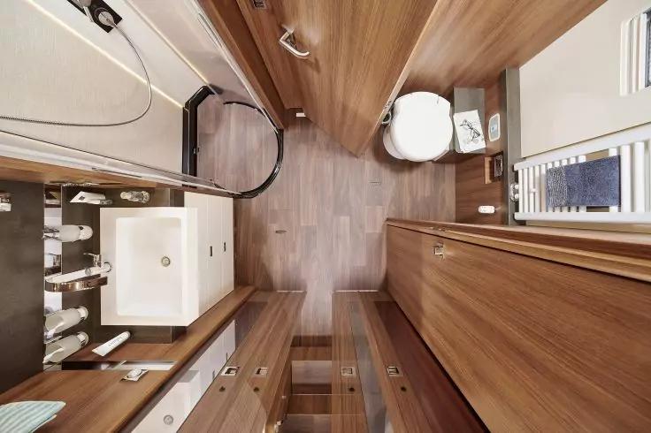 Blick von oben auf kleines Badezimmer mit Holzverkleidung, Toilette rechts, Waschbecken links, Schrankfronten und Duschabtrennung