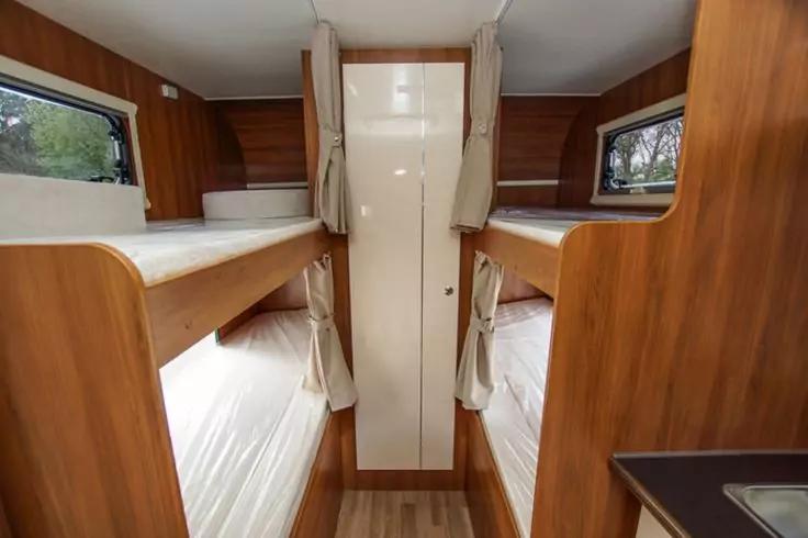 Innenraum mit zwei gegen&uuml;berliegenden Etagenbetten, Holzverkleidung, Vorh&auml;nge an den Betten und kleine Fenster