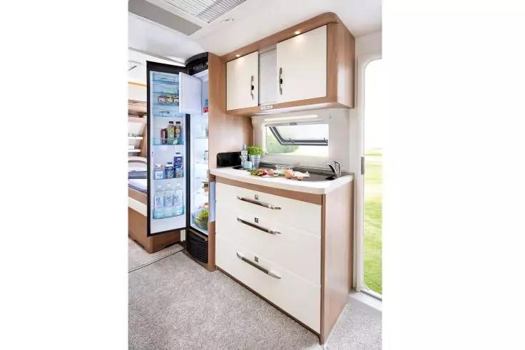 Innenbereich mit K&uuml;chenzeile, offenem K&uuml;hlschrank, Arbeitsfl&auml;che mit Sp&uuml;le, Schneidebrett und Gem&uuml;se, Oberschr&auml;nken und Schubladen