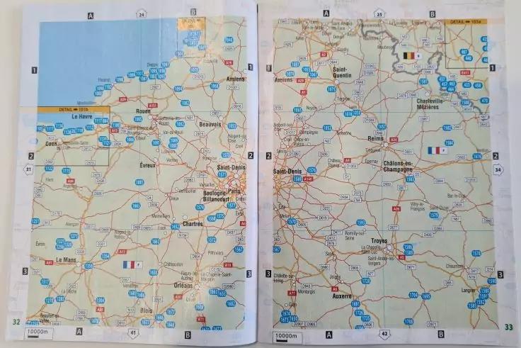 Aufgeschlagenes Atlasblatt mit zwei Seiten; Kartenansicht mit St&auml;dten, Stra&szlig;en, blauen Symbolen und kleinen Flaggen; hellblaue Fl&auml;che oben links; Mittelfalz sichtbar