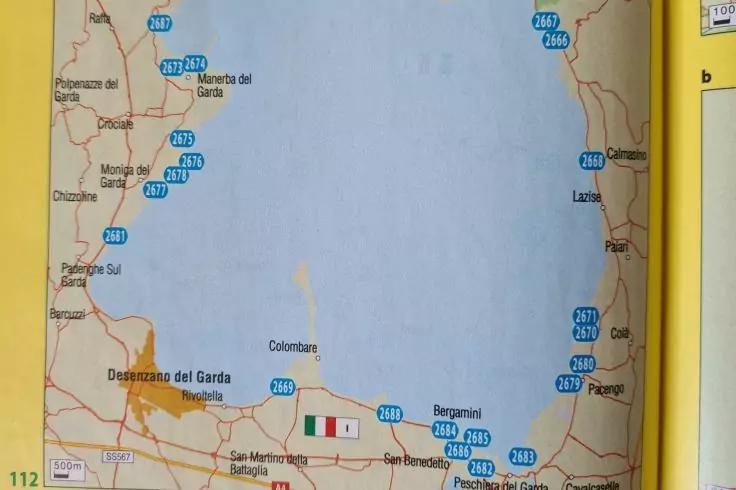 Foto einer gedruckten Karte: gro&szlig;es Gew&auml;sser, Ortsnamen (u. a. &bdquo;Desenzano del Garda&ldquo;), Stra&szlig;en, blaue Routensymbole, kleine italienische Flagge unten, gelber Seitenrand